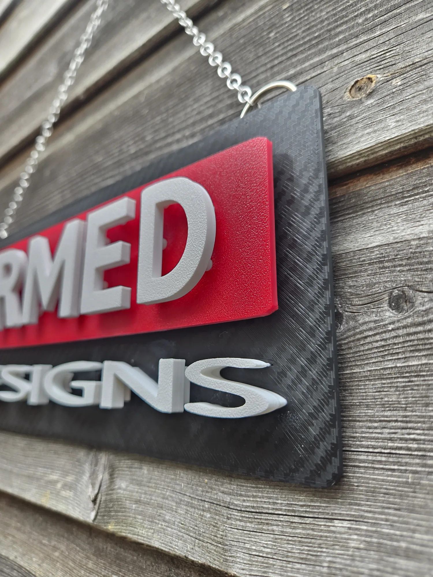 Angled view of the ArmMed Designs sign showing the carbon-textured front surface.