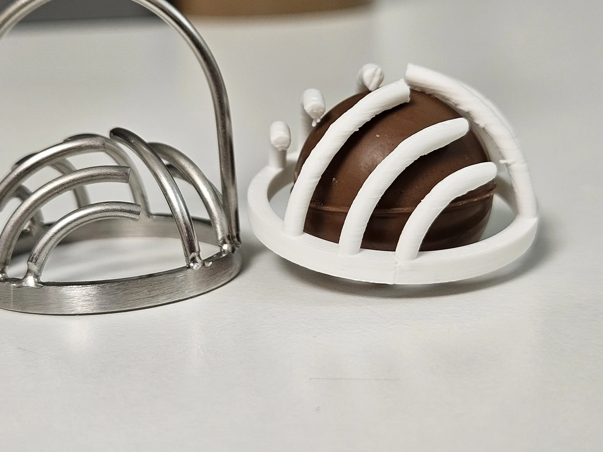 Stainless-steel decorating tool beside a white PLA prototype surrounding a real chocolate sample.