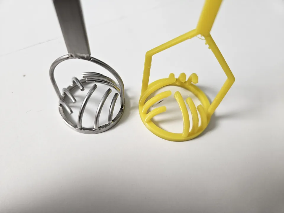 Metal tool and yellow PETG prototype viewed from above on a white table.