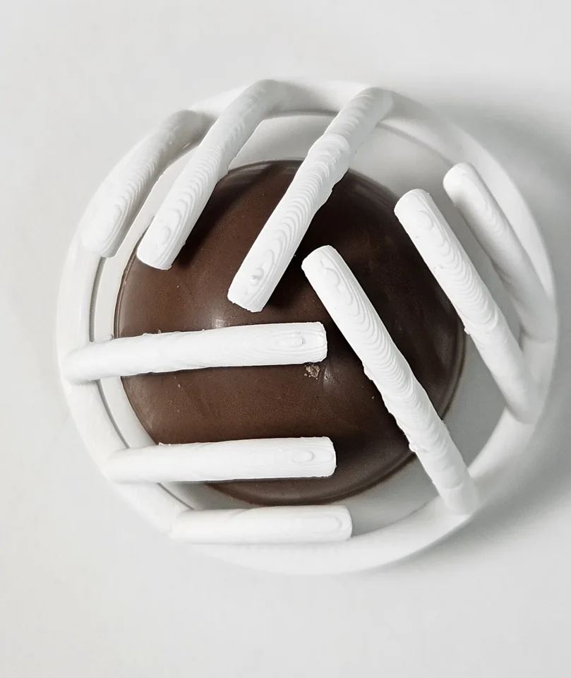 Top view of a white PLA prototype fitted over a round chocolate sample.