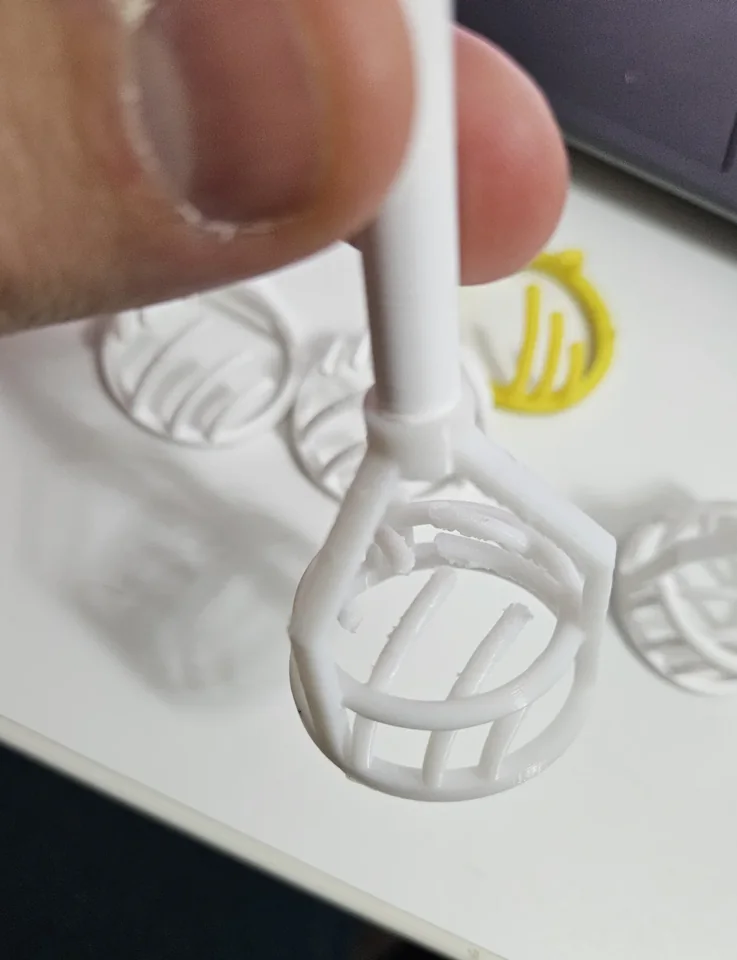 Reinforced white prototype held by its handle, showing three supports around the head.