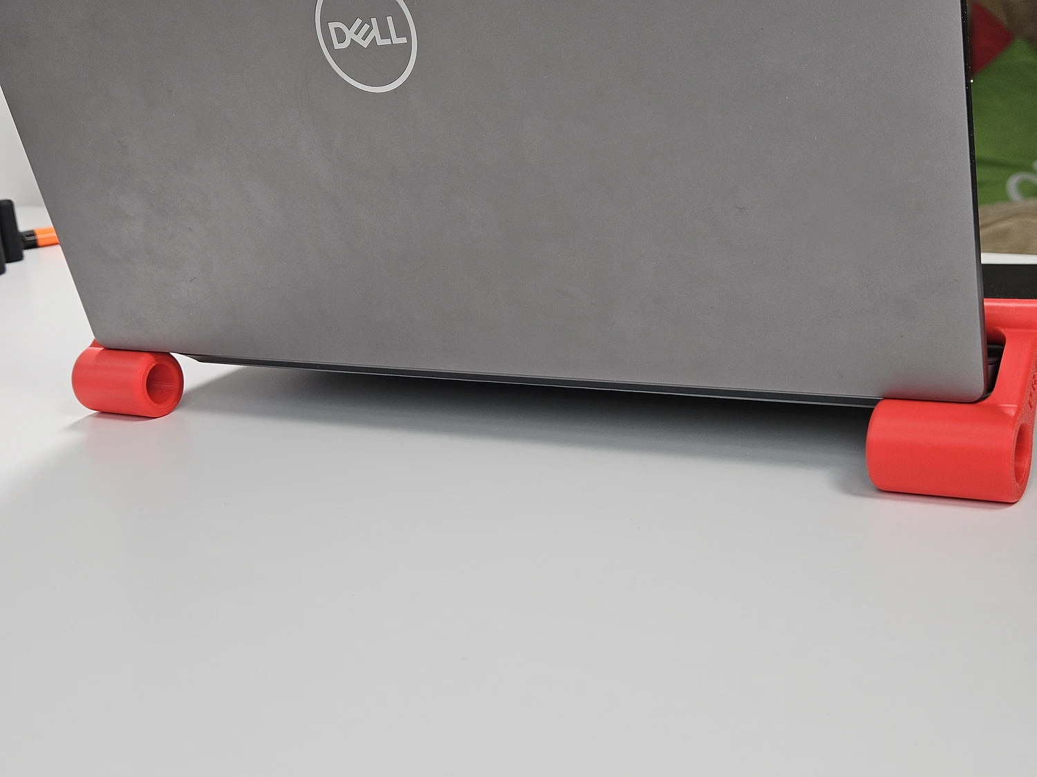Laptop standing on a pair of red clip-on riser feet viewed from the rear.