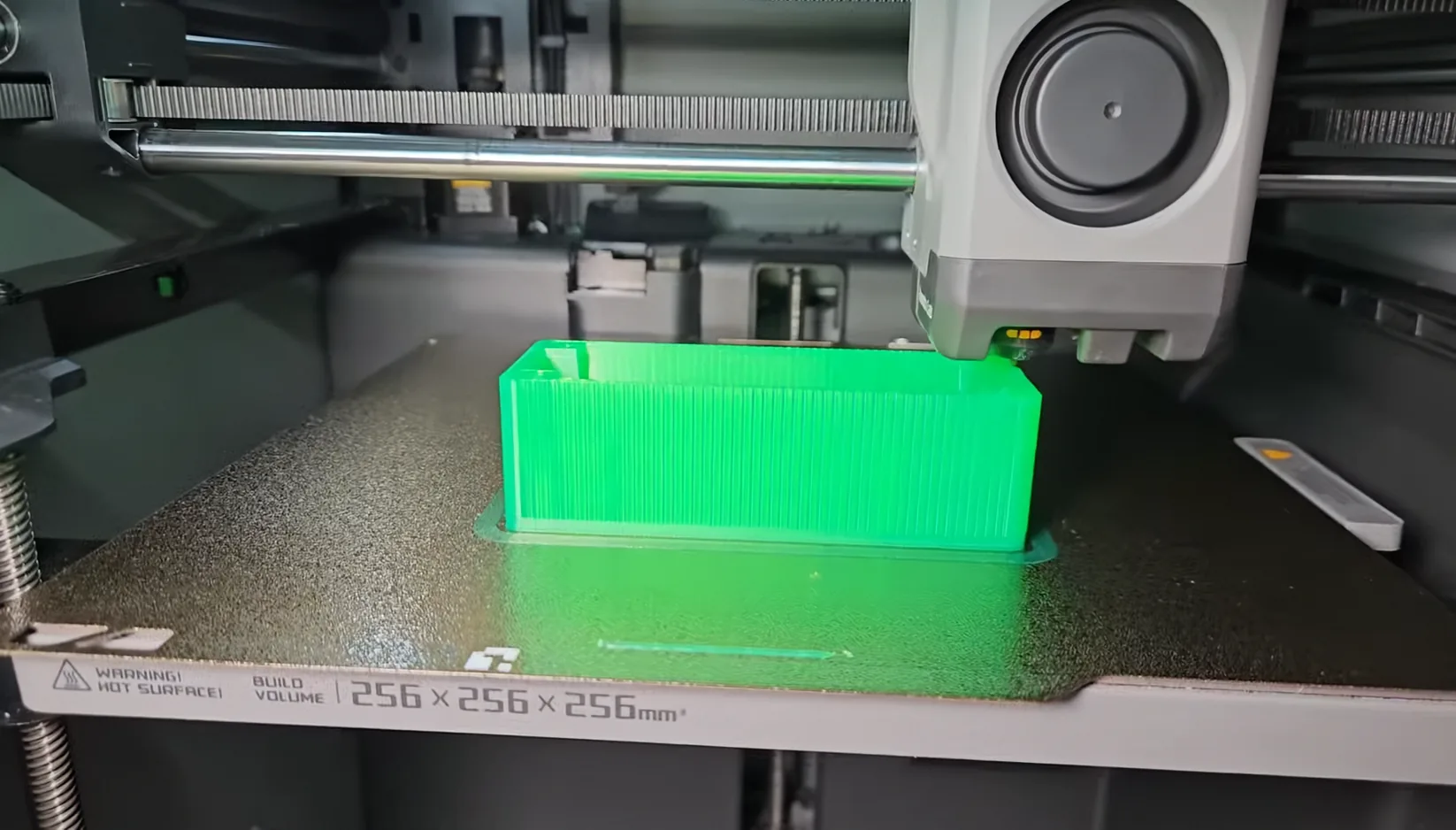 A translucent green test enclosure printing inside a 3D printer.