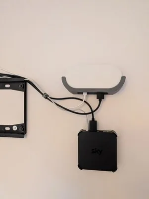 Google TV Streamer mounted beside a television bracket, with cables and a separate black device below.