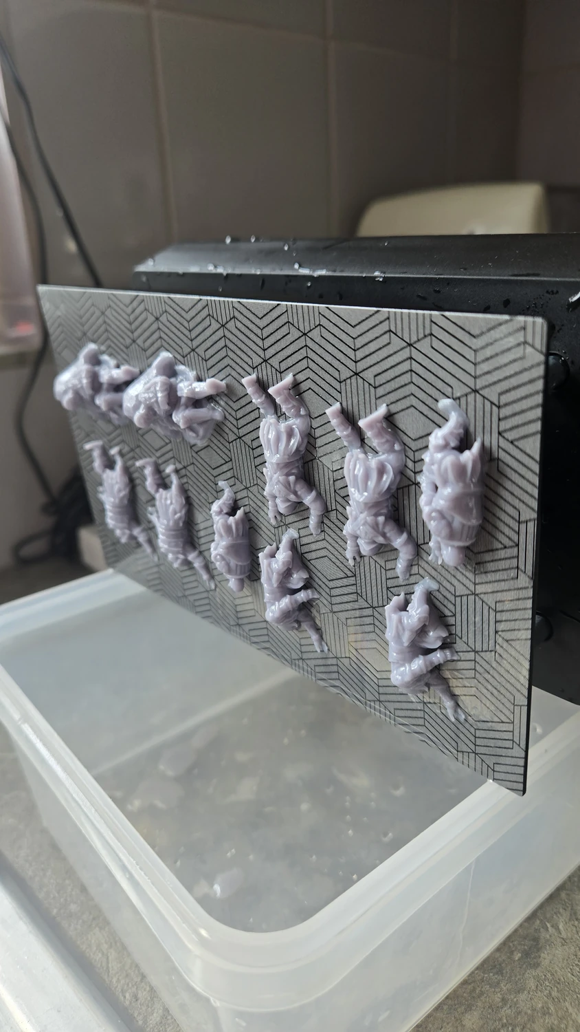 Several small orc miniatures attached to the build plate of a resin printer.