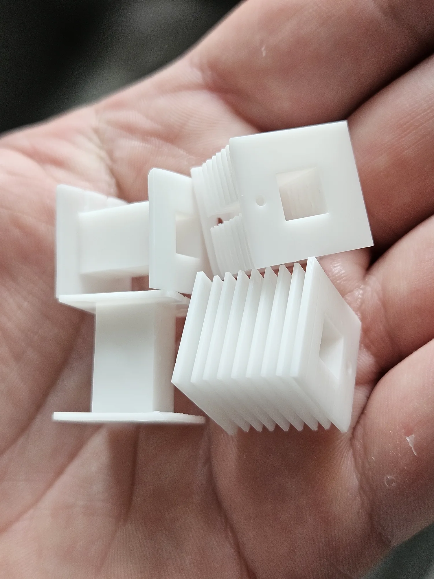 Rectangular resin-printed coil bobbins shown in hand for scale.