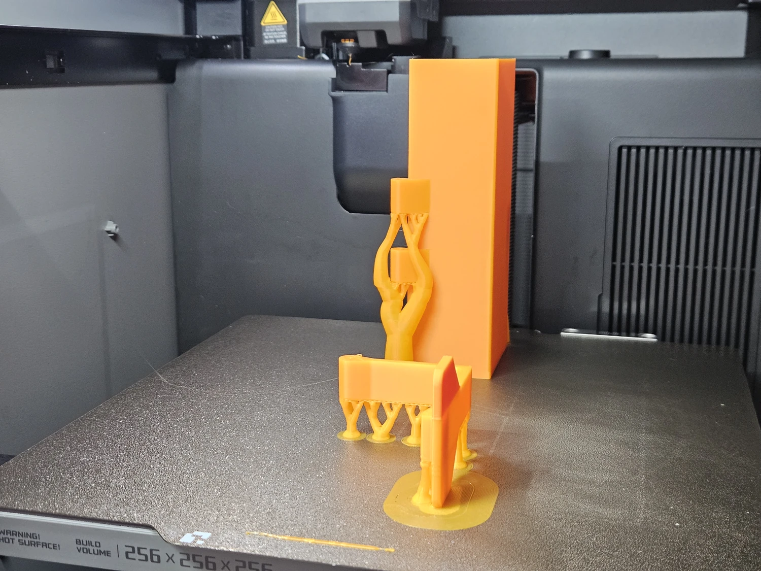Orange Ryobi battery removal aid parts being printed on the printer bed.
