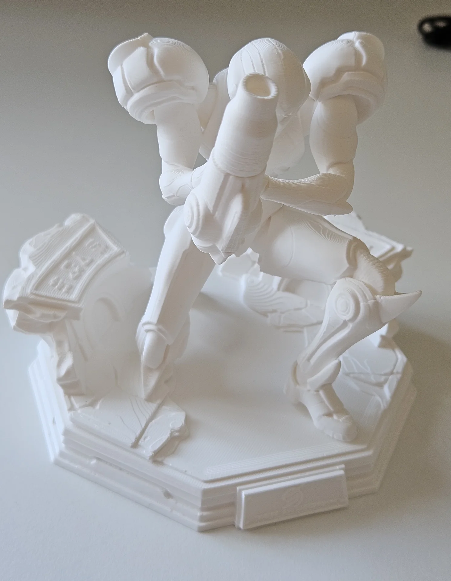 Completed white PLA+ armoured character statue with an arm cannon on a sculpted display base.
