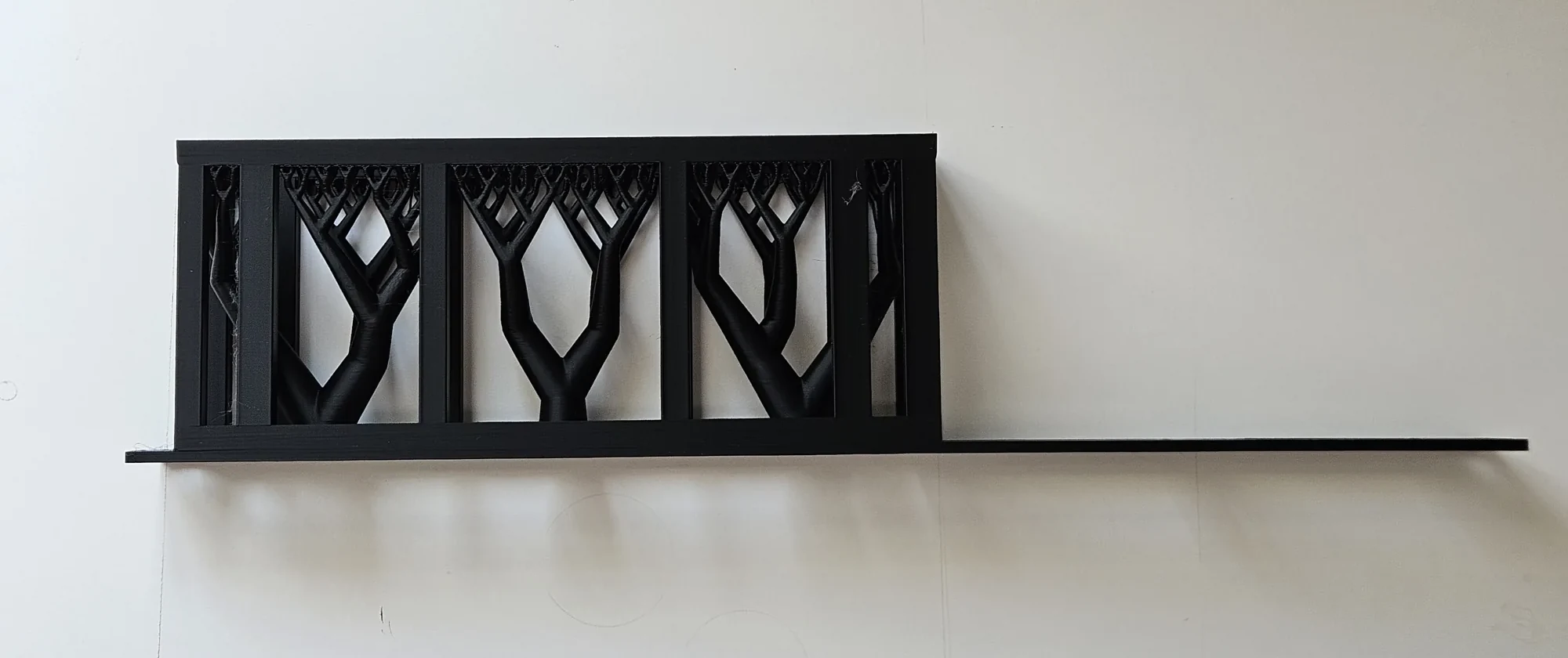 One-piece black adapter on a white table with branching support material still filling its basket.