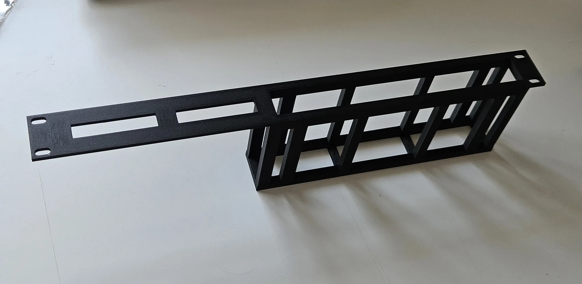 Finished black one-piece rack adapter with an open basket and slotted front panel, viewed at an angle.