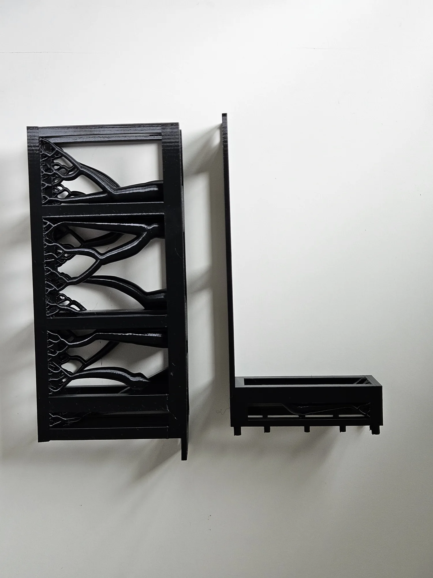 Two black sections of the original adapter on a white table, with branching supports still attached to the basket.
