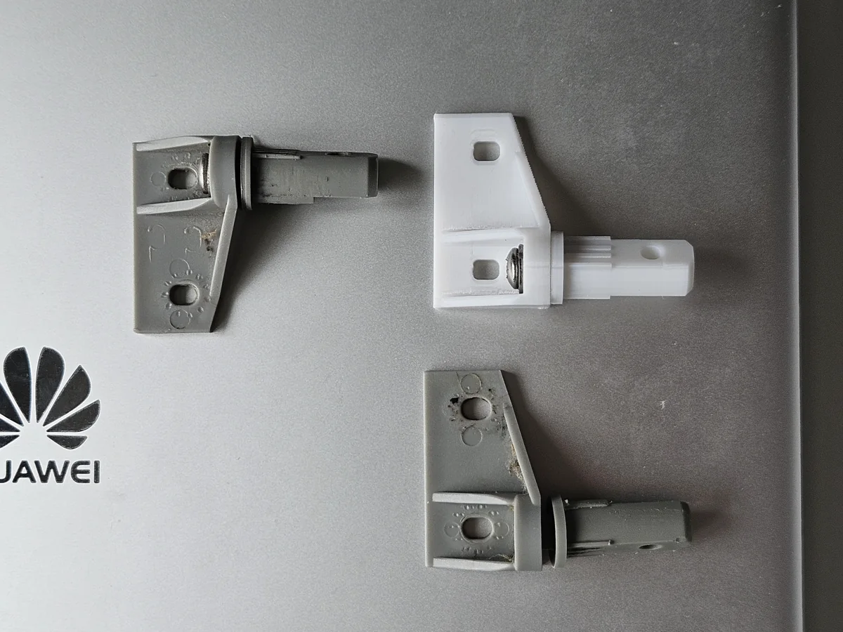 Grey original shower-door hinge beside white printed trial parts.